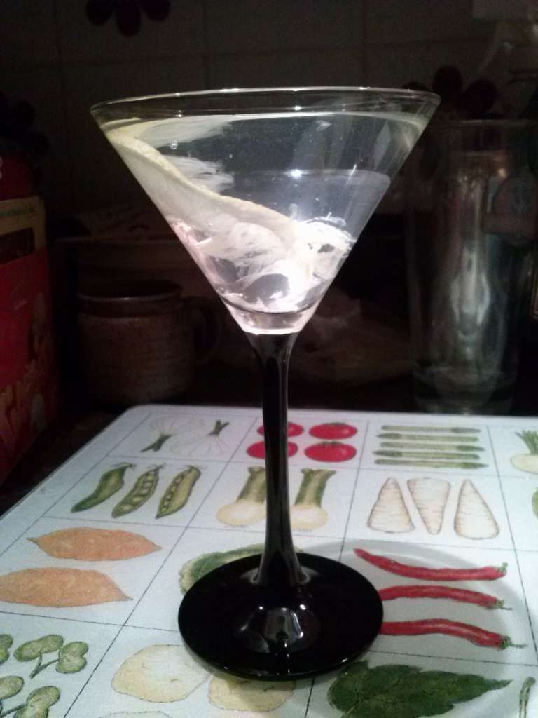 Martini glass on my glass cutting board appears to glow with some gloppy white substance in the gin.